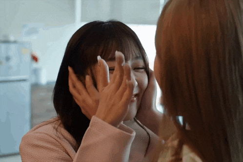 two women are touching each other 's faces and one has a ring on her finger