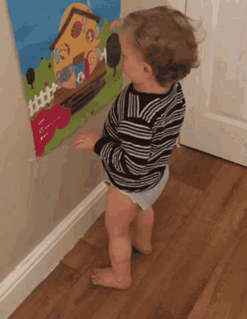 a baby in a diaper stands in front of a picture of a house on the wall