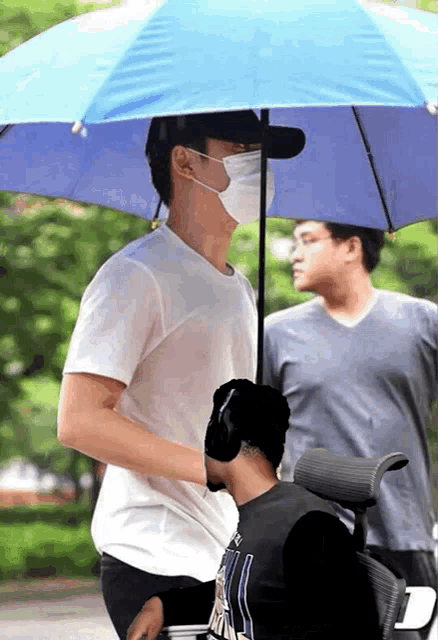 a man wearing a mask is holding an umbrella over another man in a wheelchair