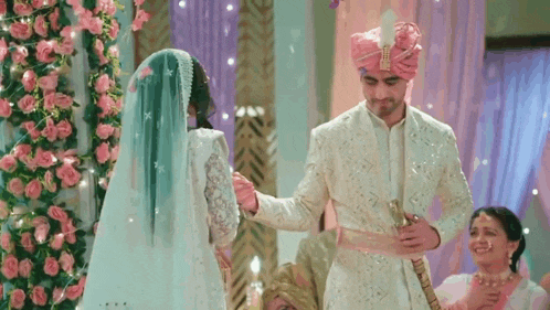 a bride and groom are standing next to each other in a room with flowers in the background .