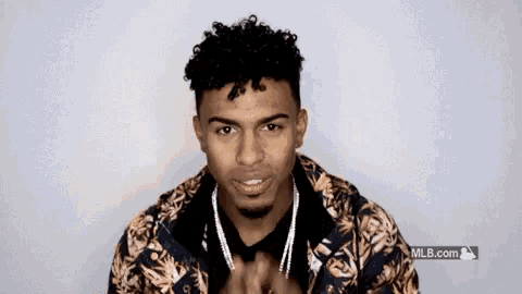 a young man with curly hair and a beard is wearing a floral jacket and necklace .