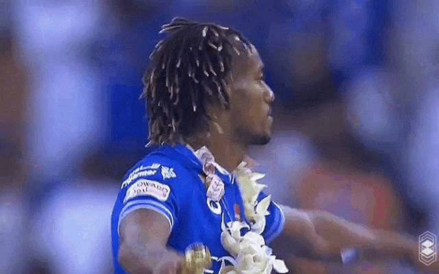 a man with dreadlocks is wearing a blue shirt and a lei .