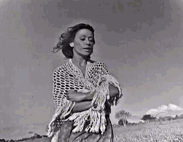 a black and white photo of a woman standing in a field with her arms crossed