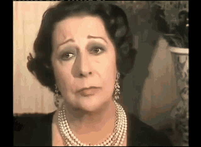 a woman is wearing a pearl necklace and earrings and making a sad face .