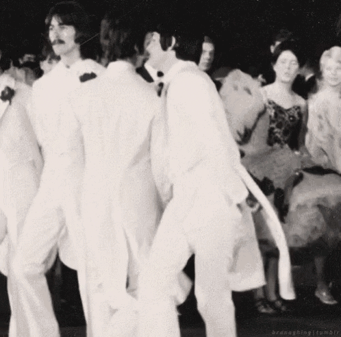 a black and white photo of two men in white suits dancing in front of a crowd .
