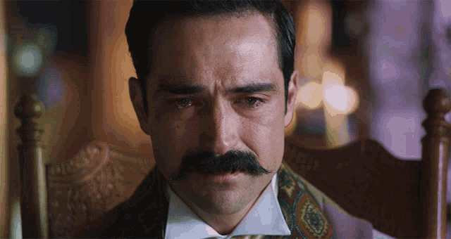 a man with a mustache is crying and sitting in a chair