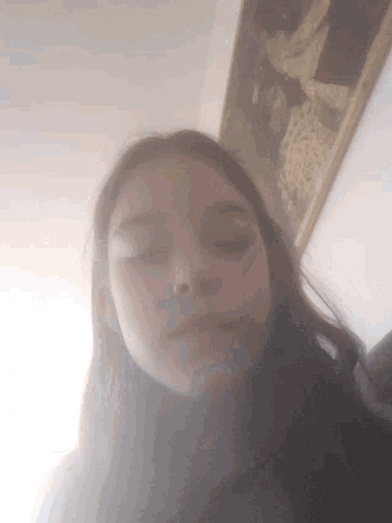 a woman is taking a selfie with her eyes closed in front of a picture on the wall .