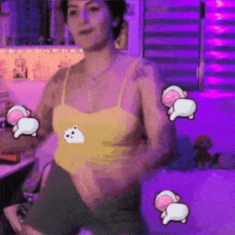 a woman in a yellow tank top is dancing in front of a purple wall