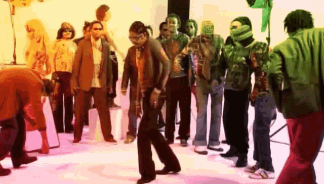 a group of people are standing in a room and one of them is wearing a green jacket