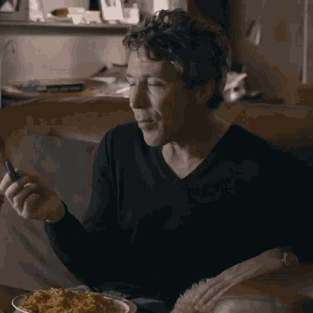 a man is sitting on a couch eating a bowl of noodles