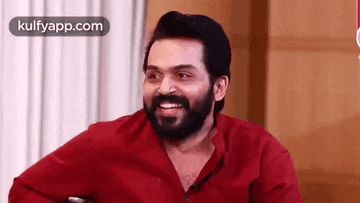 a man with a beard wearing a red shirt is smiling .