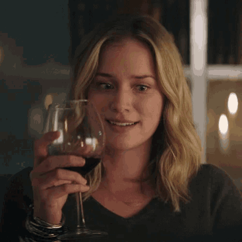 a woman is drinking a glass of red wine in a dark room .