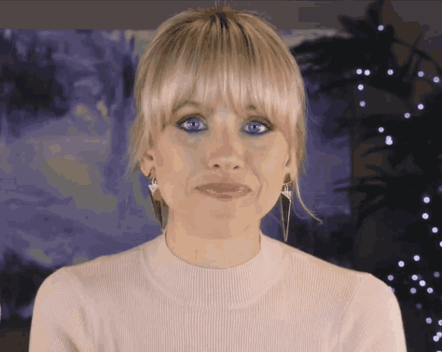 a woman with blonde hair and blue eyes is wearing a white sweater