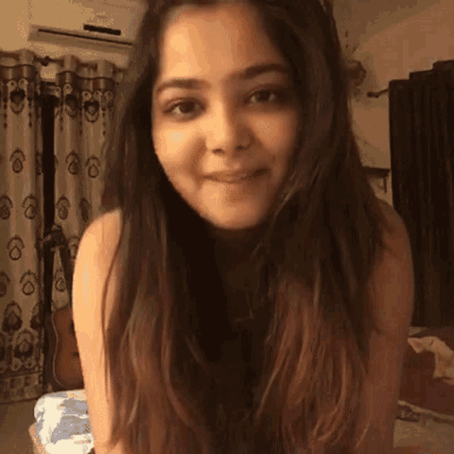a woman with long hair is sitting on a bed and smiling .
