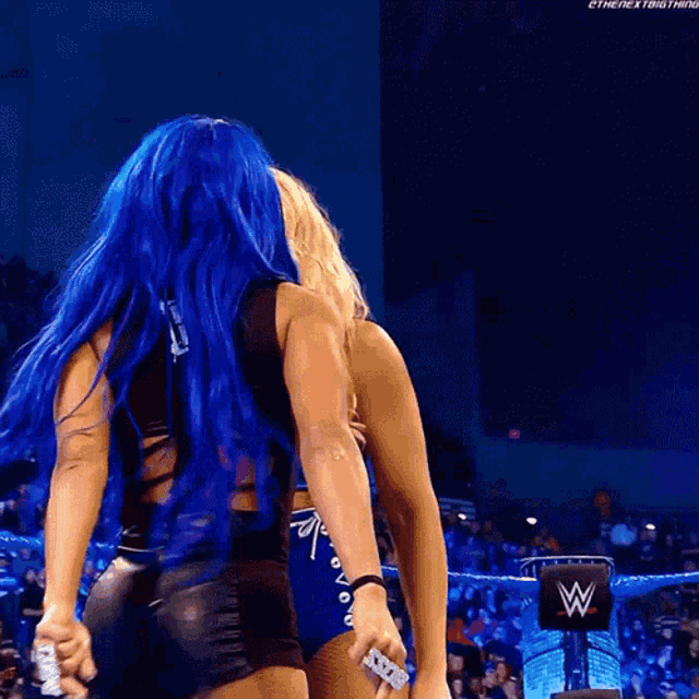 a woman with blue hair is hugging another woman in a wrestling ring .