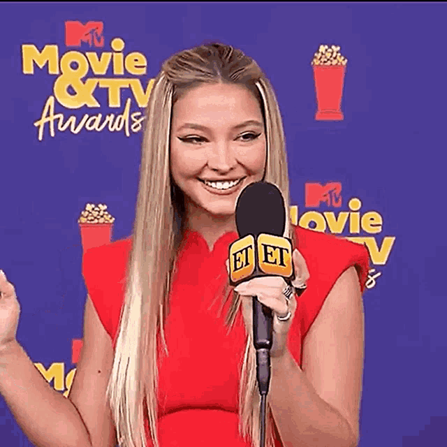 a woman in a red dress is holding a microphone and smiling at the movie and tv awards .