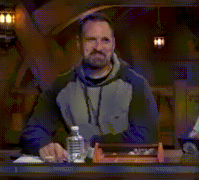 a man is sitting at a table with his arms outstretched in a dark room .