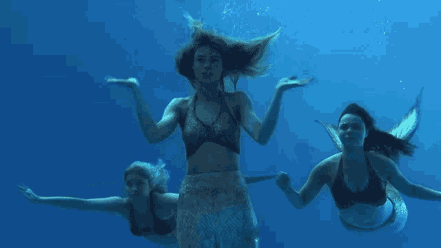 three mermaids are swimming in the ocean and holding hands