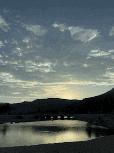 a body of water with mountains in the background and a cloudy sky
