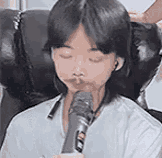 a woman is holding a microphone in her mouth while sitting in a chair with her eyes closed .