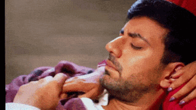 a man is laying on a bed with his eyes closed and a woman is touching his face