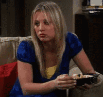 a woman in a blue shirt is sitting on a couch holding a bowl of chips .
