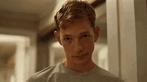a young man with red hair is looking at the camera in a room .