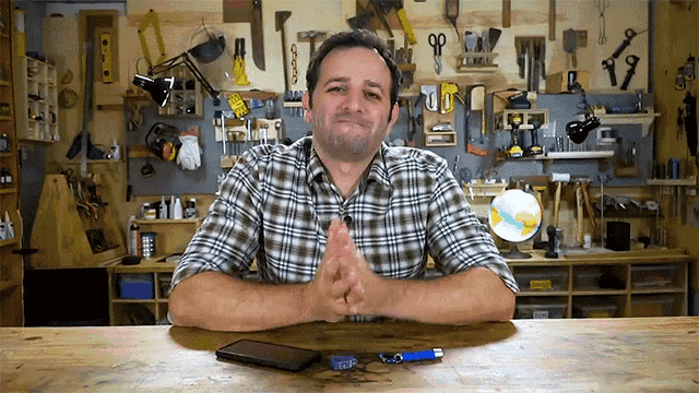 a man in a plaid shirt sits at a table in front of a workbench