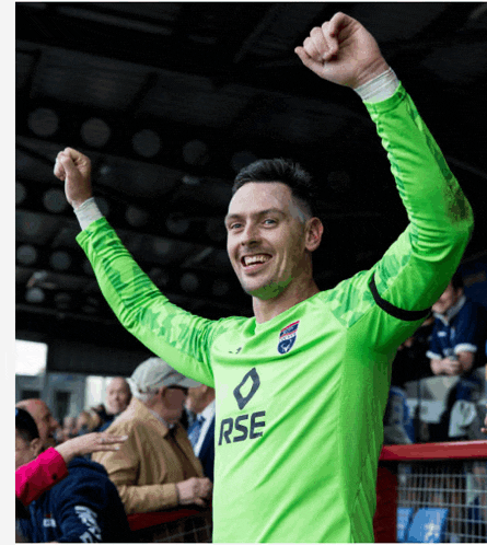 a man in a green rse jersey holds his arms up in the air