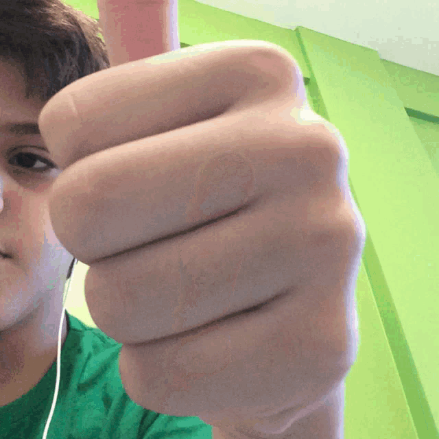 a boy in a green shirt is giving a thumbs down sign