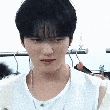 a close up of a person wearing a white tank top and necklace