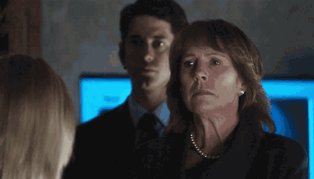 a woman with a pearl necklace stands in front of a man