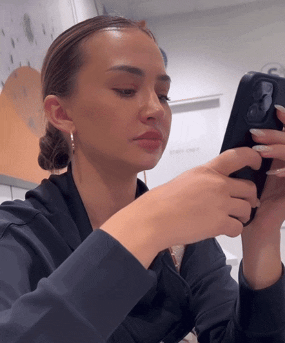 a woman in a black hoodie is holding a cell phone in her hand