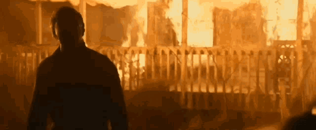 a man is standing in front of a burning building in a movie .