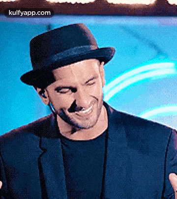 a man wearing a hat and a suit is smiling and laughing .
