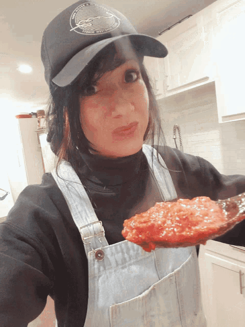 a woman wearing overalls is holding a spoonful of tomato sauce