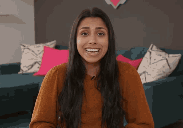 a woman in a brown sweater is smiling in front of a blue couch with pink pillows