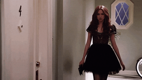 a woman in a black dress is walking in front of a door with the number 4 on it