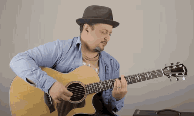 a man wearing a hat is playing an acoustic guitar made by taylor