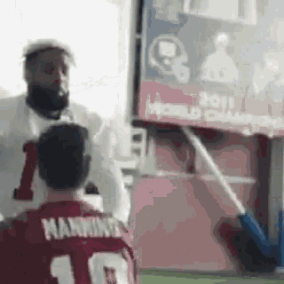 a man in a red jersey with the number 10 on it is standing next to another man in a white shirt .
