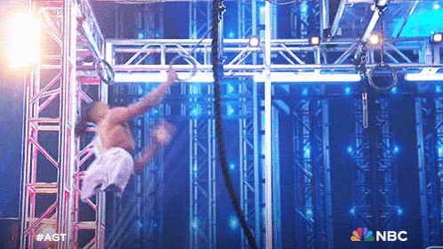a man is doing a trick on a stage with a nbc logo behind him