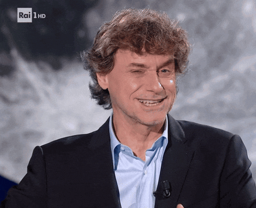 a man in a suit is smiling in front of a rai 1 hd screen
