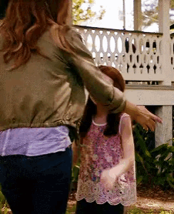 a woman in a green jacket is standing next to a little girl in a pink shirt