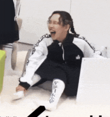 a woman in a black and white jacket is sitting on the floor laughing .