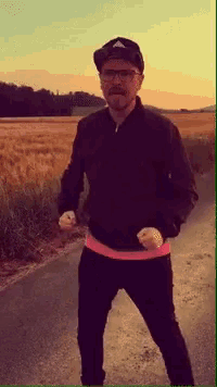 a man wearing a hat and glasses is standing on the side of a road