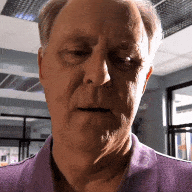 a close up of an older man 's face with a purple shirt on