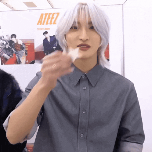 a man with long white hair is standing in front of a poster for ateez