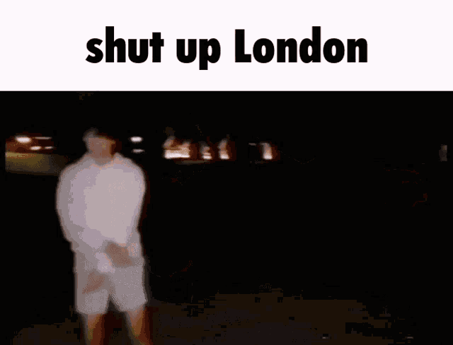 a man in a white hoodie is standing in the dark with the words `` shut up london '' above him .