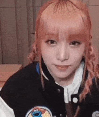 a close up of a girl with pink hair wearing a black jacket with a cookie monster on it .