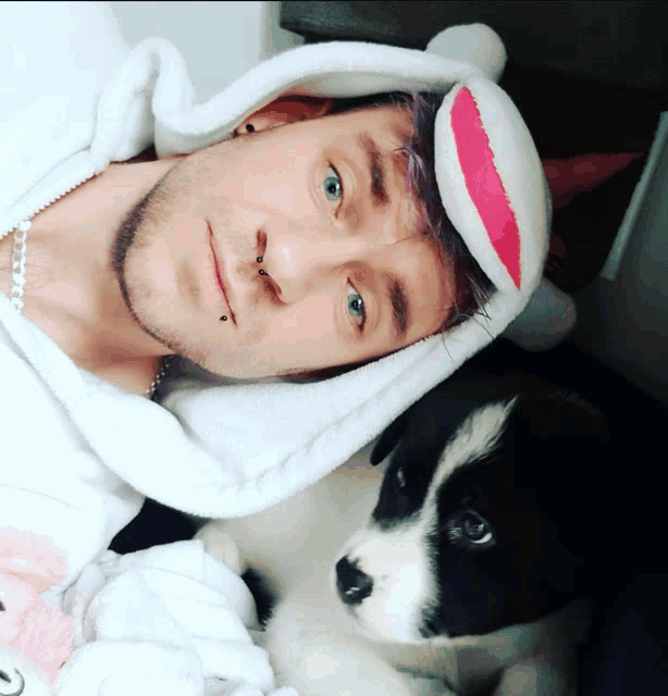 a man with purple hair and a sock on his head is laying next to a puppy